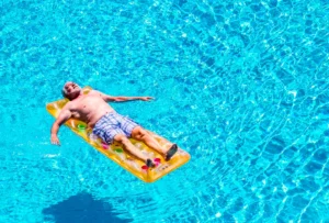 man die drijft op luchtbed in blauw water, met armen wijdt genietend van de zon